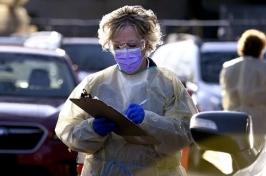 Woman in mask and gown taking information from drivers