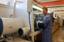 Graduate student wearing protective clothing works with his hands in a large piece of scientific equipment.